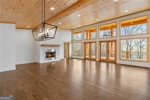 unfurnished living room featuring beamed ceiling, a towering ceiling, wood-type flooring, and an inviting chandelier