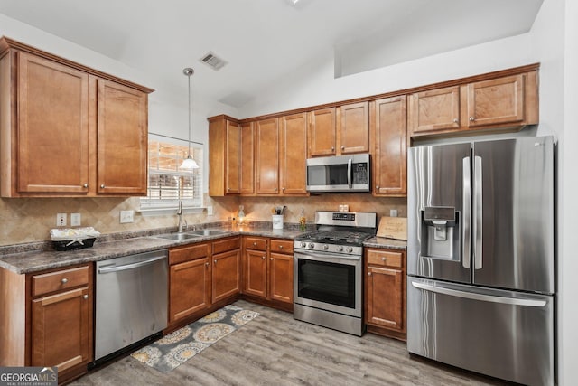 kitchen with sink, vaulted ceiling, hanging light fixtures, appliances with stainless steel finishes, and decorative backsplash