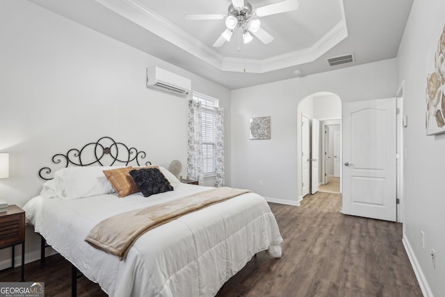 bedroom featuring an AC wall unit, wood-type flooring, ornamental molding, ceiling fan, and a raised ceiling