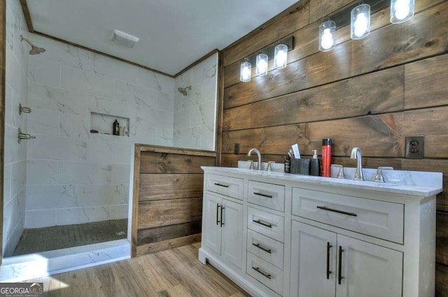 bathroom featuring tiled shower, vanity, wooden walls, and wood-type flooring