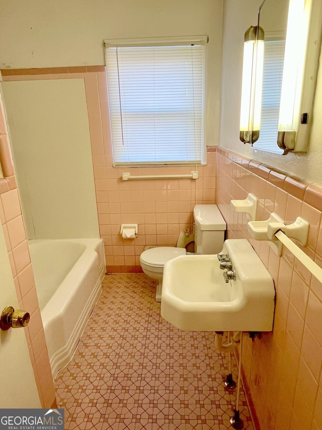 bathroom featuring toilet, sink, tile walls, a tub, and tile patterned flooring