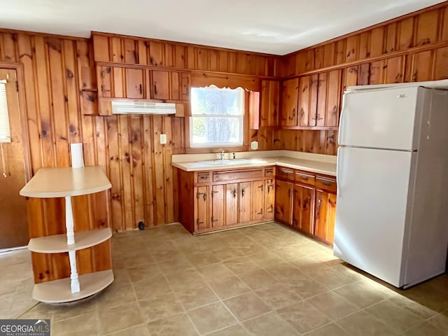 kitchen with white fridge, sink, and wood walls