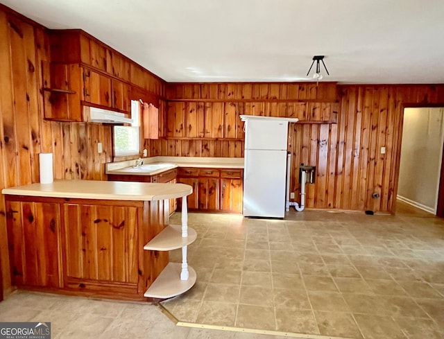 kitchen featuring white refrigerator, sink, wooden walls, and kitchen peninsula