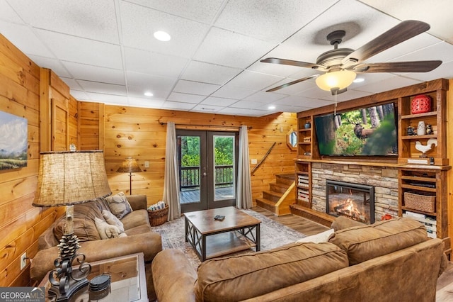 living room featuring french doors, a paneled ceiling, a fireplace, and wood walls