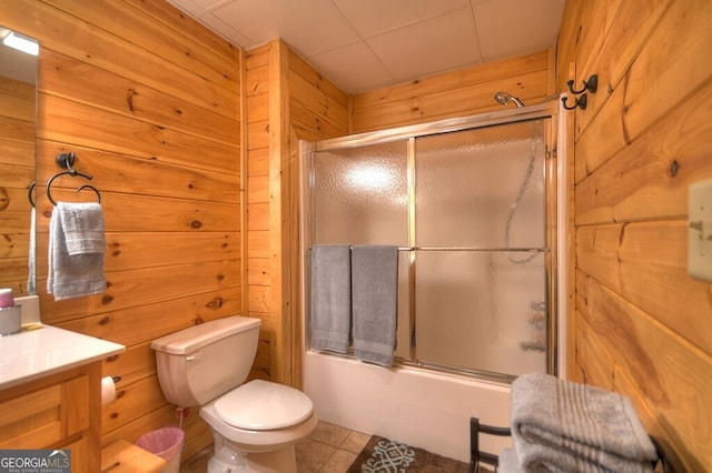 full bathroom with wooden walls, enclosed tub / shower combo, vanity, toilet, and tile patterned floors