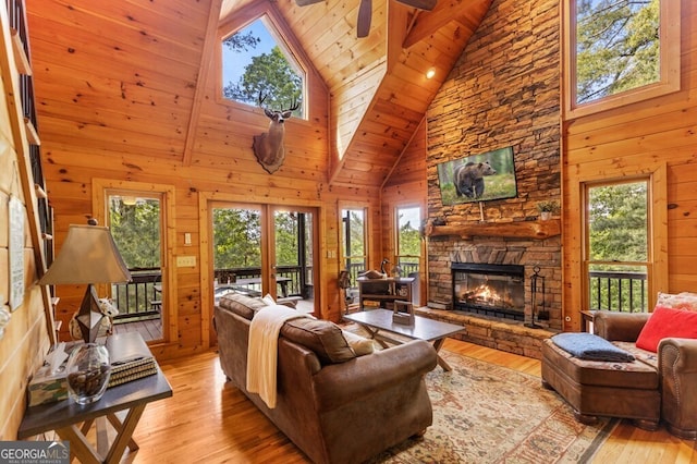 living room featuring a stone fireplace, high vaulted ceiling, wood walls, wood ceiling, and light wood-type flooring