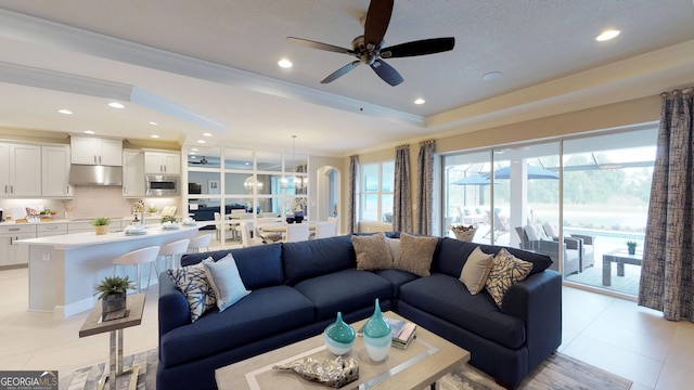 living room featuring light tile patterned floors, ornamental molding, a raised ceiling, and ceiling fan