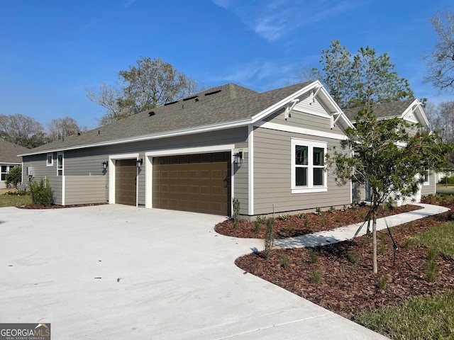 view of side of property with concrete driveway, roof with shingles, and an attached garage