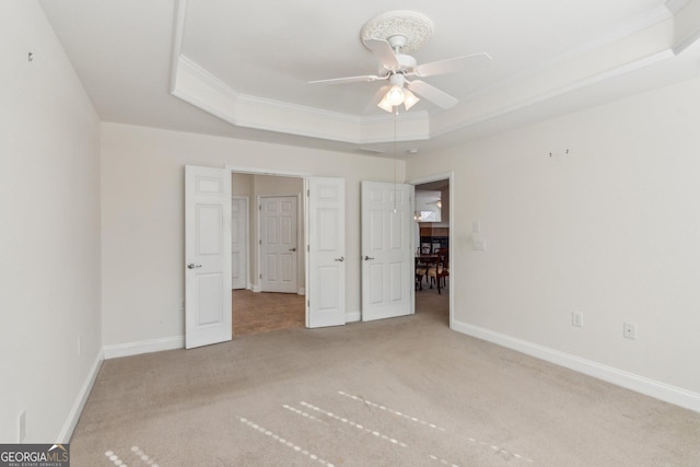 unfurnished bedroom featuring a tray ceiling, carpet floors, ornamental molding, and ceiling fan