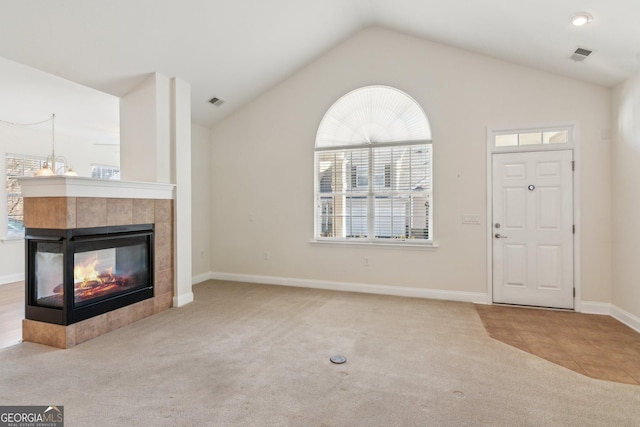 unfurnished living room with light carpet, a tiled fireplace, and vaulted ceiling