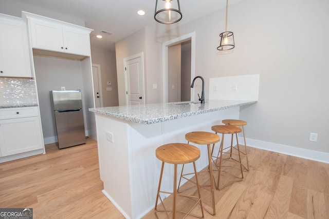 69 Oakhurst Trl, Sharpsburg, GA 30277 - kitchen featuring freestanding refrigerator, light wood-style floors, light stone counters, white cabinetry, and a kitchen bar