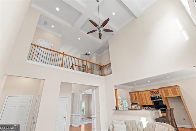 living room featuring ceiling fan, beam ceiling, a high ceiling, coffered ceiling, and ornate columns