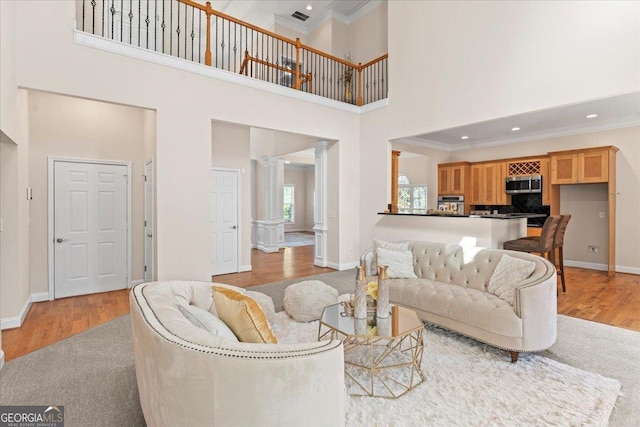 living room featuring crown molding, a towering ceiling, decorative columns, and light hardwood / wood-style floors