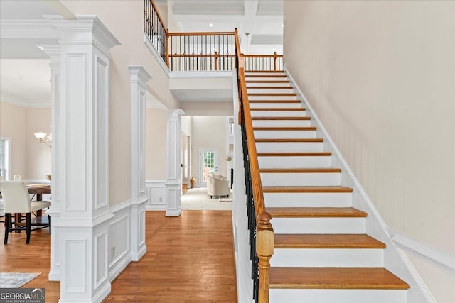 stairs with ornate columns, a chandelier, ornamental molding, beam ceiling, and hardwood / wood-style floors