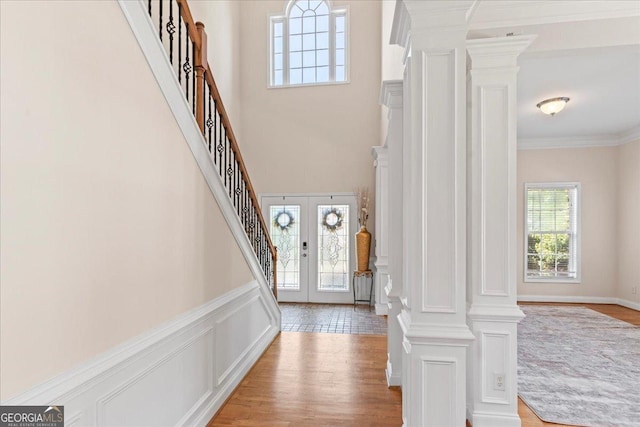 entrance foyer featuring crown molding, decorative columns, french doors, and light wood-type flooring