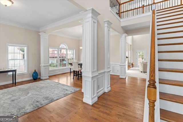 entrance foyer featuring decorative columns, ornamental molding, and light hardwood / wood-style floors