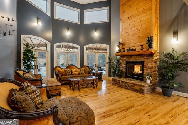 living room featuring french doors, a stone fireplace, light hardwood / wood-style floors, and a high ceiling