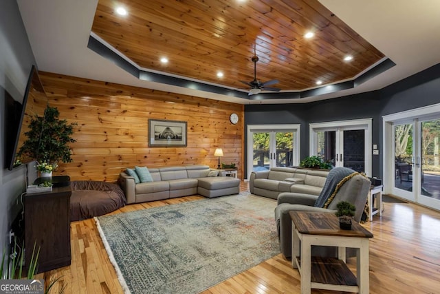 living room featuring wooden walls, a healthy amount of sunlight, a raised ceiling, wooden ceiling, and french doors