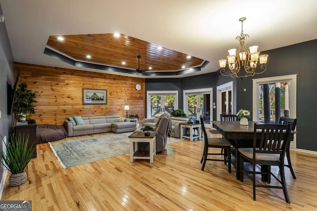 dining room featuring a tray ceiling, wooden walls, wooden ceiling, and light hardwood / wood-style floors