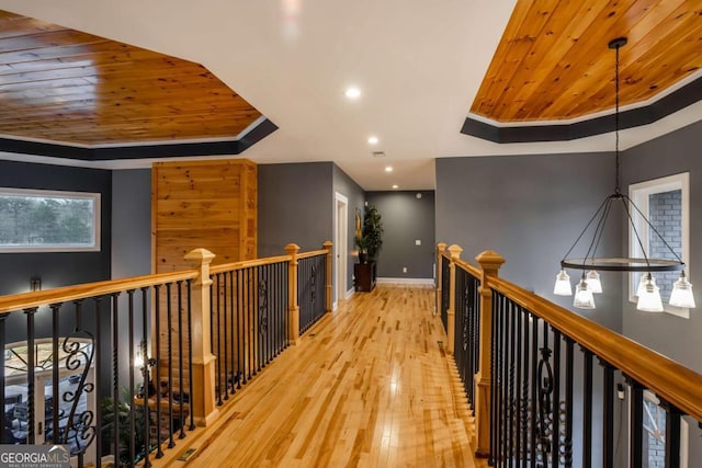 hall with a tray ceiling, ornamental molding, wooden ceiling, and light hardwood / wood-style floors