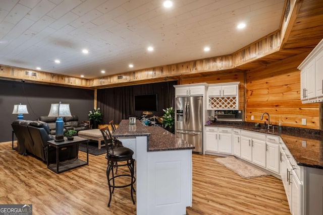 kitchen featuring stainless steel refrigerator with ice dispenser, sink, a kitchen island, dark stone counters, and white cabinets