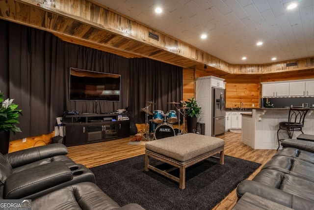 living room featuring light wood-type flooring, sink, and wooden walls