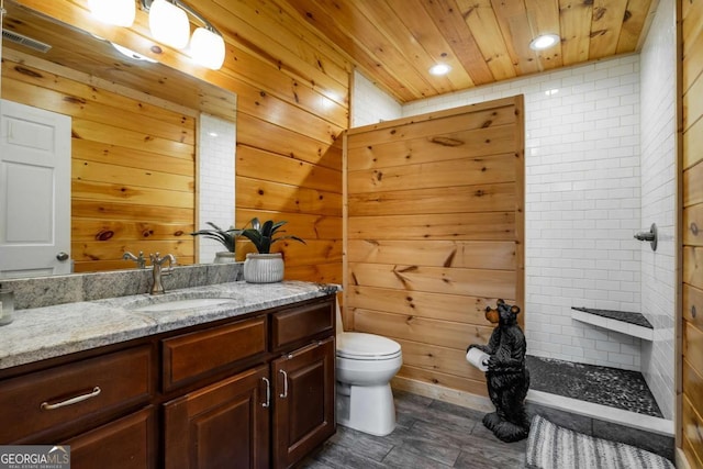 bathroom with toilet, vanity, wooden walls, and a tile shower