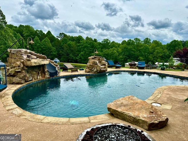 view of pool featuring an outdoor fire pit, a water slide, and a patio area