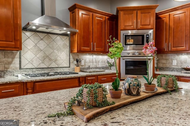 kitchen with stainless steel appliances, backsplash, light stone counters, and wall chimney exhaust hood