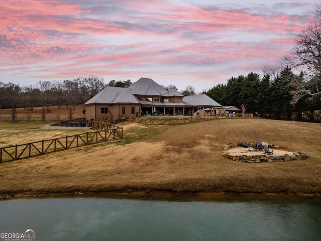 view of front of house with an outdoor fire pit, a lawn, and a water view