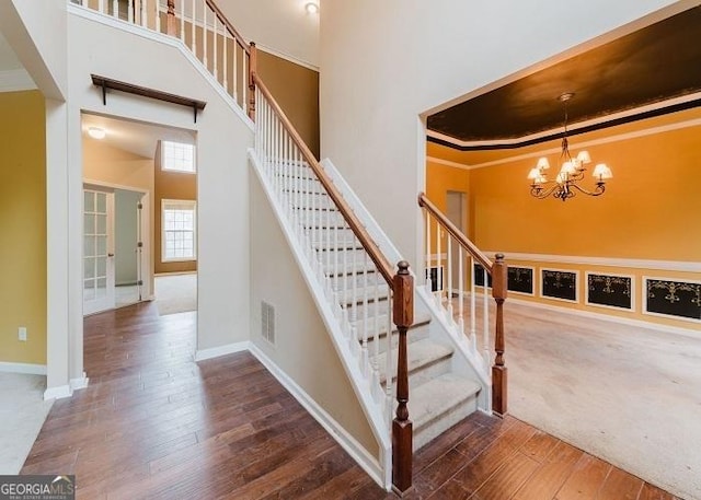 stairway with a high ceiling, ornamental molding, hardwood / wood-style floors, and a notable chandelier