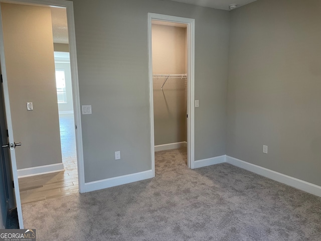 unfurnished bedroom featuring a walk in closet, light colored carpet, and a closet