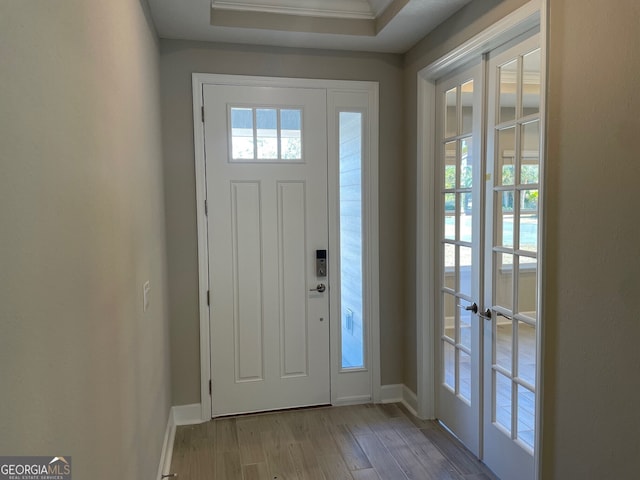 entrance foyer with a raised ceiling, ornamental molding, and light hardwood / wood-style flooring