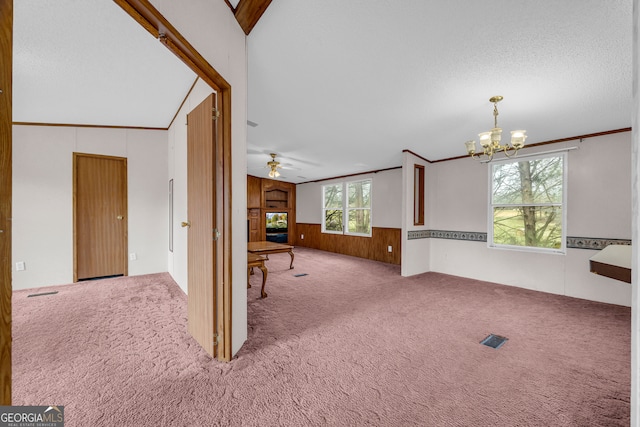 carpeted empty room with crown molding, a healthy amount of sunlight, ceiling fan with notable chandelier, and wood walls