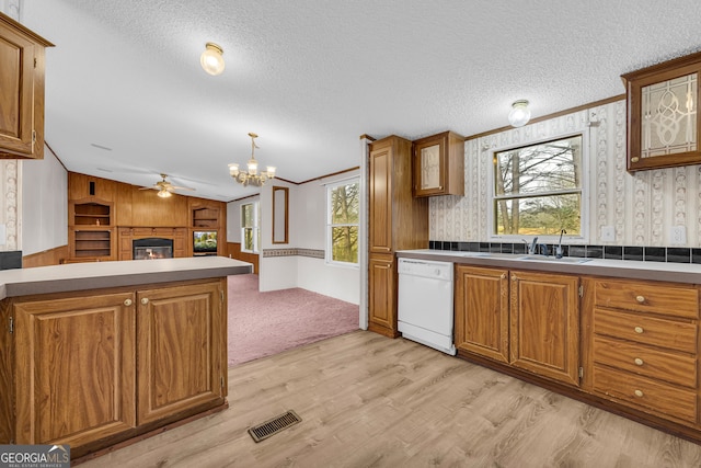 kitchen with decorative light fixtures, dishwasher, sink, a textured ceiling, and light wood-type flooring