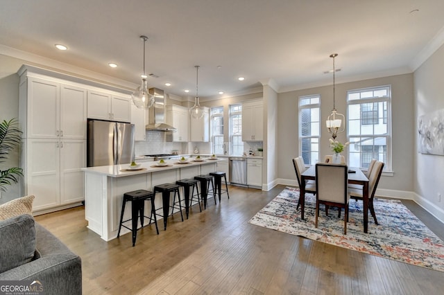 kitchen featuring a kitchen island, appliances with stainless steel finishes, white cabinets, hanging light fixtures, and wall chimney exhaust hood