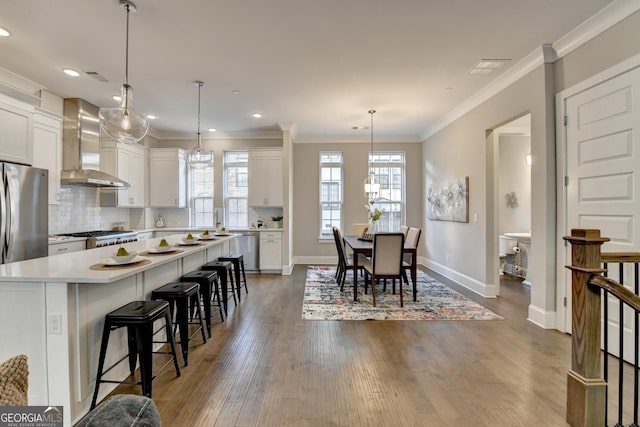 kitchen featuring a kitchen island, appliances with stainless steel finishes, decorative light fixtures, white cabinetry, and wall chimney range hood