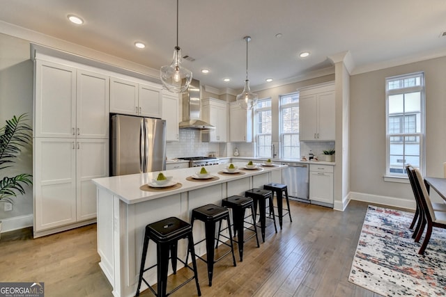 kitchen with a kitchen island, appliances with stainless steel finishes, white cabinets, hanging light fixtures, and wall chimney exhaust hood