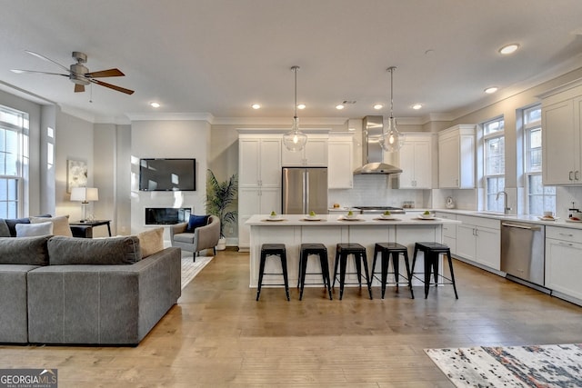 kitchen with a breakfast bar area, hanging light fixtures, stainless steel appliances, a kitchen island, and wall chimney exhaust hood