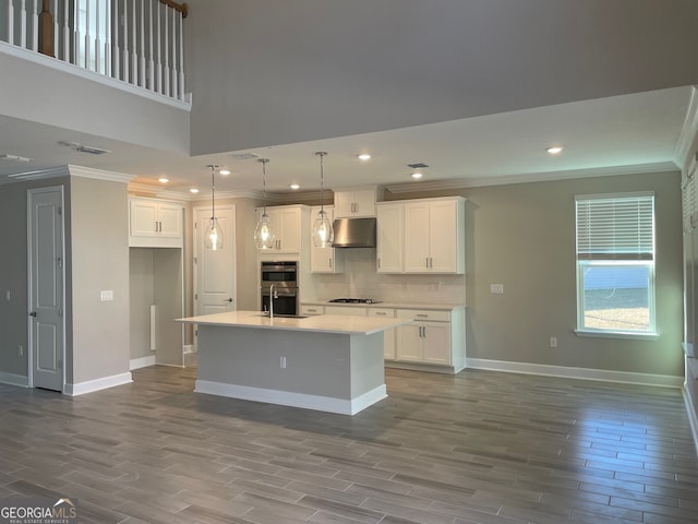 kitchen with pendant lighting, appliances with stainless steel finishes, white cabinets, a center island with sink, and decorative backsplash