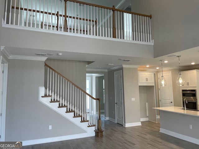 staircase featuring hardwood / wood-style flooring, ornamental molding, and a high ceiling