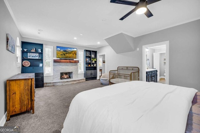 carpeted bedroom featuring ceiling fan, ensuite bathroom, a fireplace, and ornamental molding