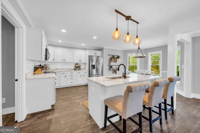 kitchen featuring pendant lighting, sink, white cabinetry, stainless steel appliances, and a center island with sink