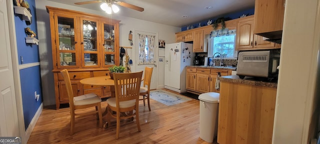 kitchen featuring sink, backsplash, white refrigerator with ice dispenser, ceiling fan, and light hardwood / wood-style floors