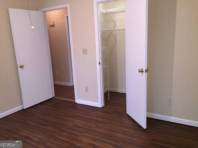 unfurnished bedroom with a closet, dark hardwood / wood-style floors, and a spacious closet