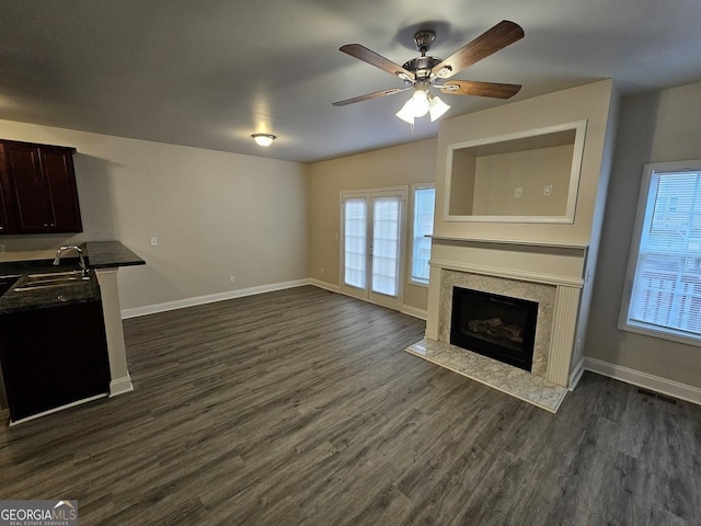 unfurnished living room featuring dark hardwood / wood-style flooring, sink, a premium fireplace, and ceiling fan