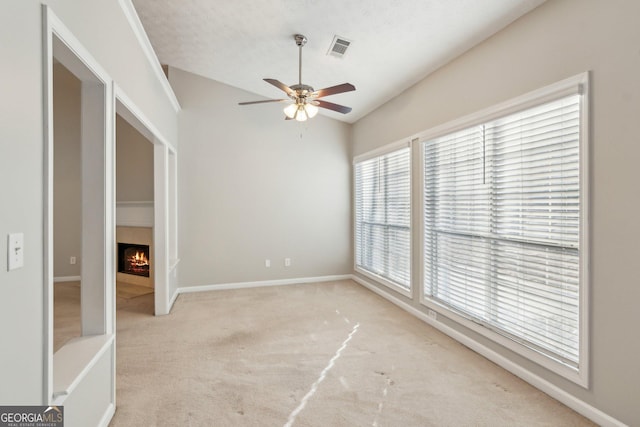 unfurnished room featuring lofted ceiling, light colored carpet, a ceiling fan, visible vents, and a lit fireplace