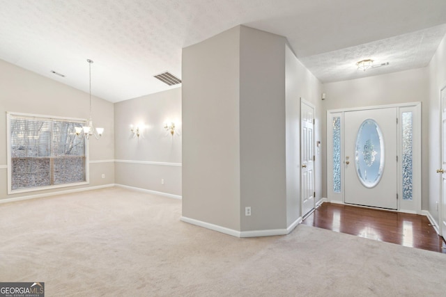 carpeted foyer entrance featuring baseboards, visible vents, lofted ceiling, a textured ceiling, and a notable chandelier