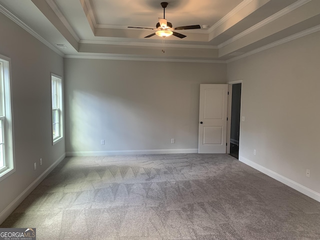 empty room with a raised ceiling, ornamental molding, light carpet, and ceiling fan