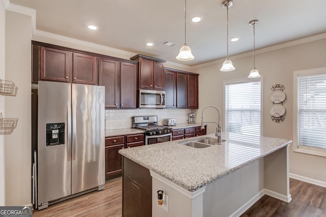 kitchen with sink, light stone counters, appliances with stainless steel finishes, pendant lighting, and a kitchen island with sink